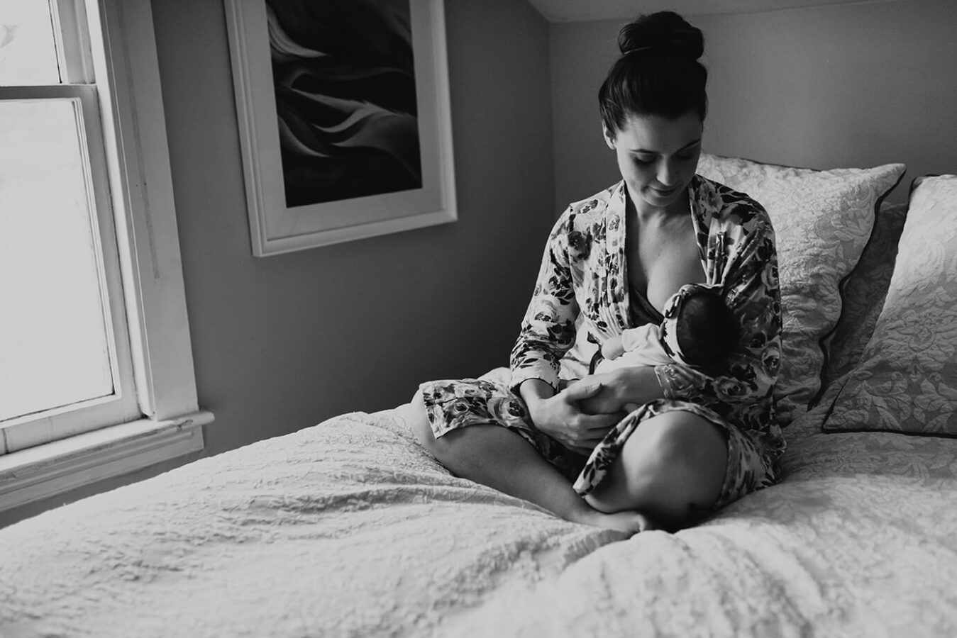 Mom breastfeeding her daughter on her bed during a newborn photography session
