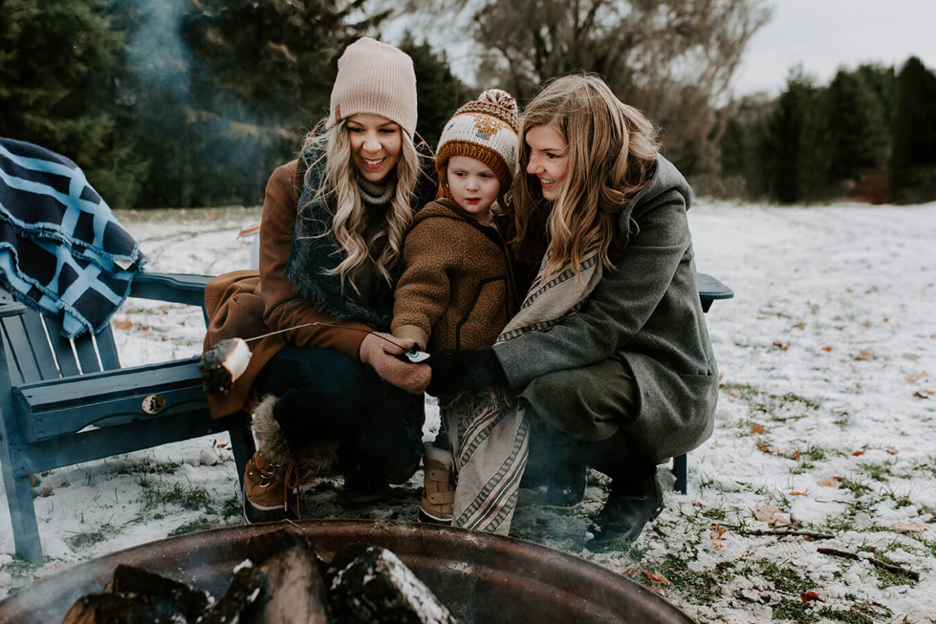 Two women and a toddler roasting marshmallows around a fire pit